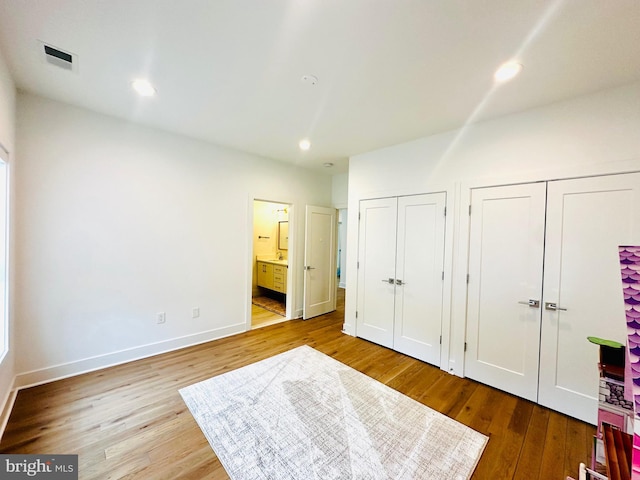 unfurnished bedroom featuring visible vents, ensuite bathroom, recessed lighting, wood finished floors, and multiple closets