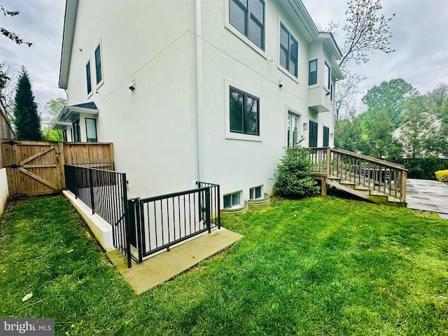 view of home's exterior with a deck, a gate, stucco siding, fence, and a yard