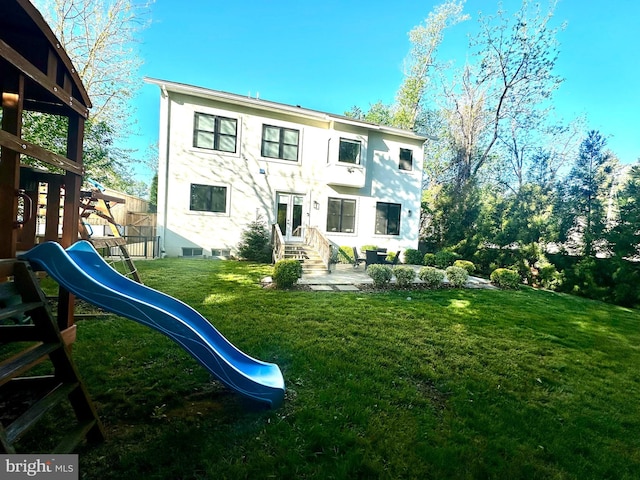 rear view of property featuring fence, entry steps, a playground, stucco siding, and a lawn