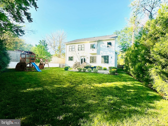 rear view of property with a lawn, fence, stucco siding, and a playground