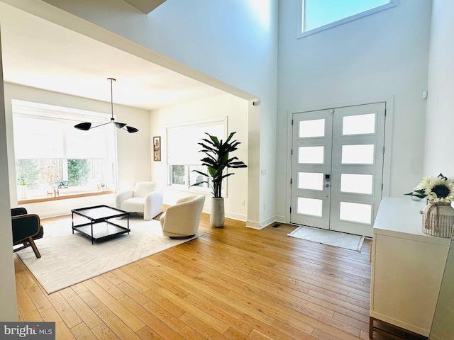 foyer with baseboards, light wood-style floors, french doors, and a towering ceiling