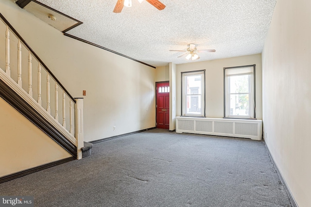 unfurnished living room featuring a textured ceiling, carpet flooring, radiator heating unit, a ceiling fan, and stairs