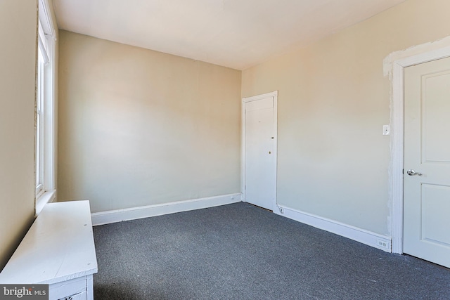 spare room with baseboards and dark carpet