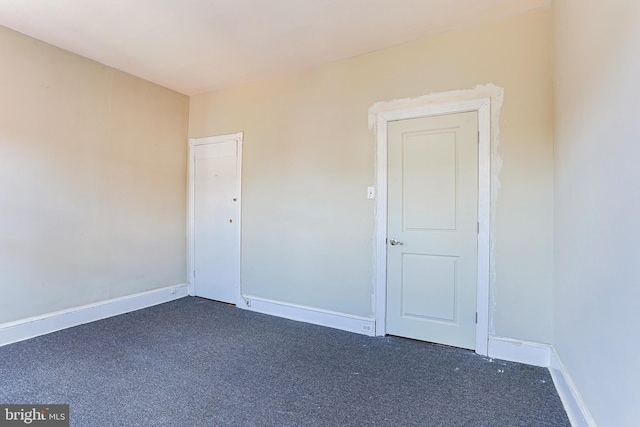 unfurnished room featuring dark carpet and baseboards