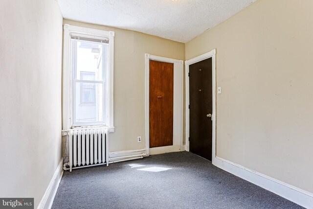 spare room featuring baseboards, radiator, a textured ceiling, and dark carpet