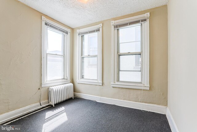 unfurnished room with radiator heating unit, baseboards, carpet flooring, and a textured ceiling
