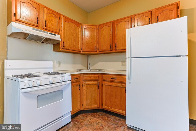 kitchen with a sink, light countertops, under cabinet range hood, white appliances, and brown cabinetry
