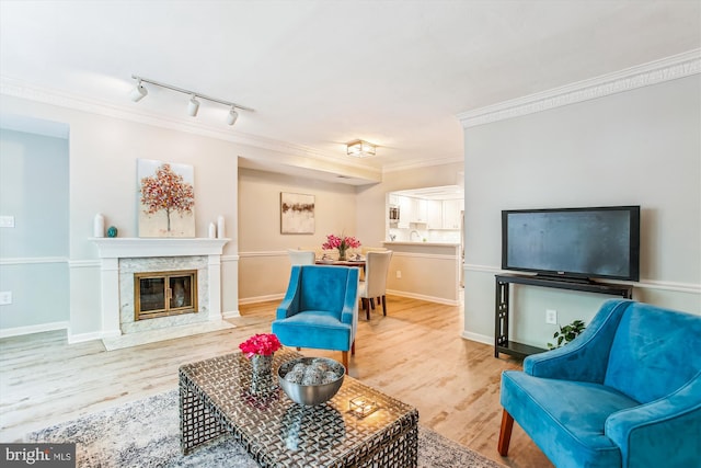 living room featuring crown molding, track lighting, a premium fireplace, baseboards, and wood finished floors
