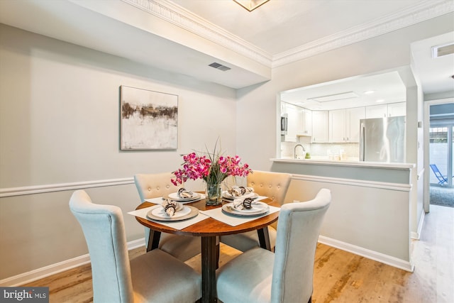 dining space with visible vents, light wood-style flooring, crown molding, and baseboards