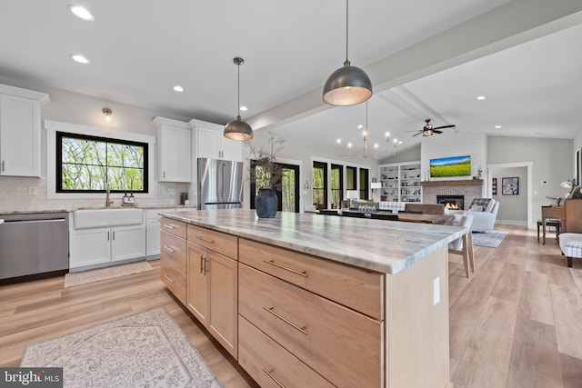 kitchen with light stone countertops, a sink, a large fireplace, stainless steel appliances, and backsplash