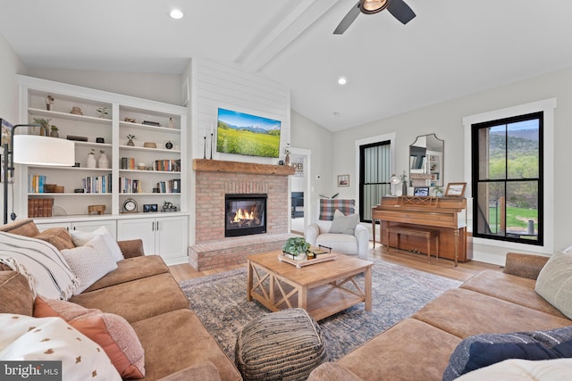 living room featuring ceiling fan, lofted ceiling with beams, light wood finished floors, a fireplace, and recessed lighting