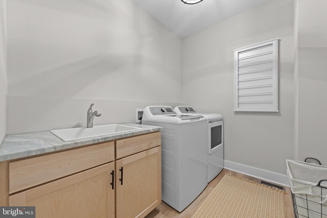 laundry area featuring independent washer and dryer, visible vents, light wood-type flooring, cabinet space, and a sink