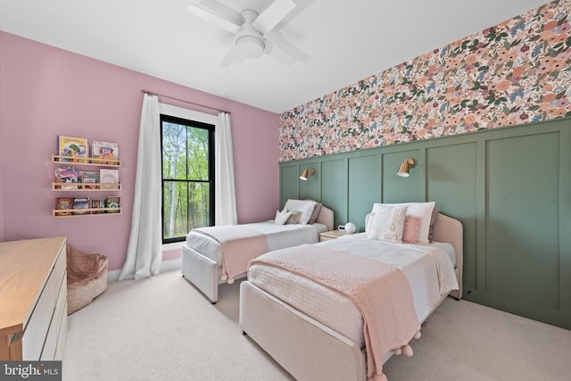 bedroom featuring light colored carpet, wainscoting, a decorative wall, a ceiling fan, and wallpapered walls