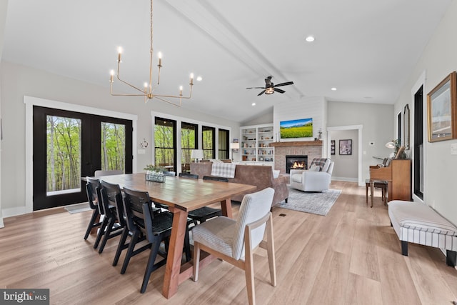 dining area with lofted ceiling with beams, a glass covered fireplace, french doors, light wood-style flooring, and ceiling fan with notable chandelier