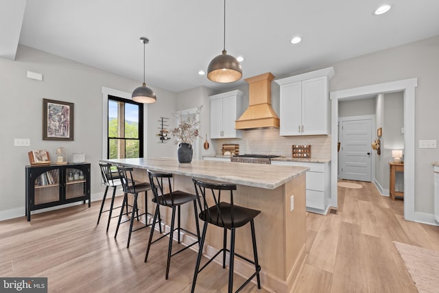kitchen with backsplash, a center island, white cabinetry, custom exhaust hood, and light wood-style flooring
