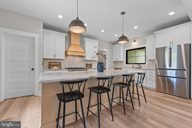 kitchen with a kitchen island, a sink, premium range hood, white cabinets, and freestanding refrigerator