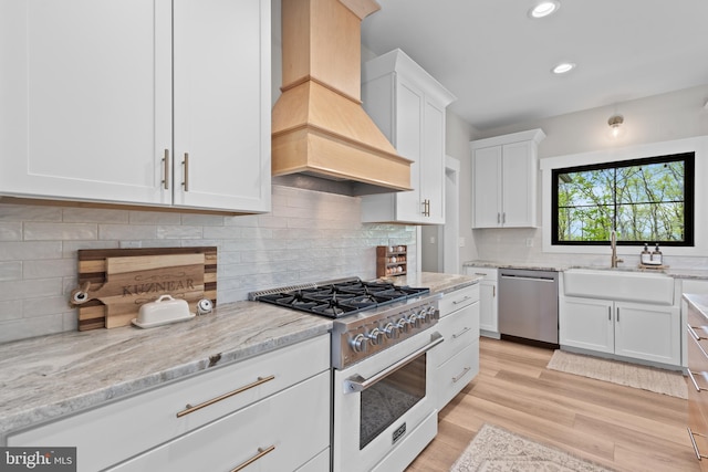 kitchen with range with gas stovetop, white cabinetry, custom range hood, a sink, and dishwasher