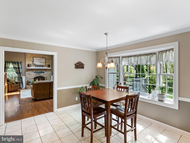 dining space featuring a chandelier, a brick fireplace, light tile patterned flooring, baseboards, and ornamental molding