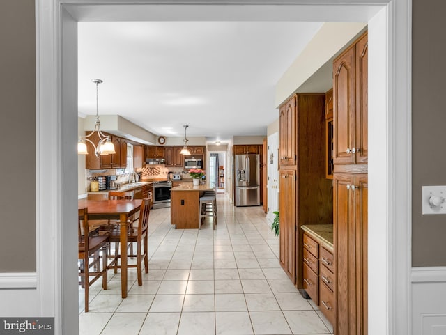 kitchen with brown cabinets, a breakfast bar, stainless steel appliances, a center island, and under cabinet range hood