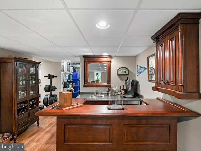 bar with a paneled ceiling, light wood finished floors, wet bar, and a sink