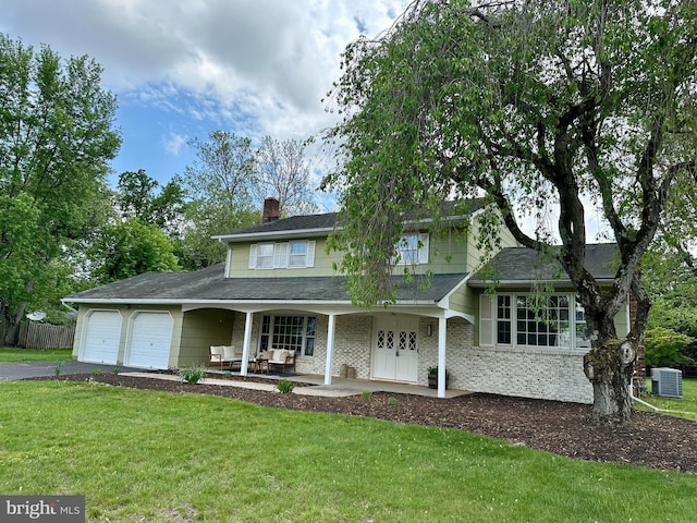 view of front of house featuring covered porch, an attached garage, aphalt driveway, central AC unit, and a front yard