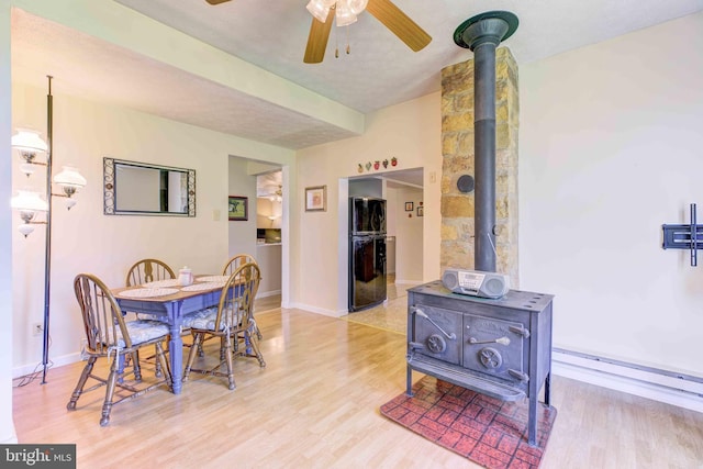 dining space featuring a wood stove, light wood-type flooring, a ceiling fan, and baseboards