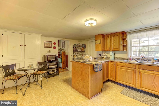 kitchen featuring a sink, a peninsula, brown cabinetry, open shelves, and light flooring
