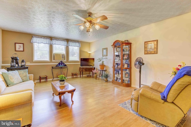 living room with a textured ceiling, wood finished floors, ceiling fan, cooling unit, and baseboards