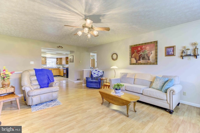 living area featuring a textured ceiling, light wood-type flooring, a ceiling fan, and baseboards