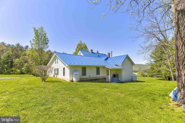 back of property with a lawn, metal roof, a chimney, and a standing seam roof