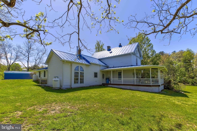 back of house featuring a standing seam roof, a yard, a chimney, and metal roof