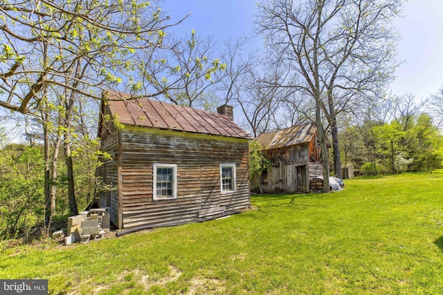 view of home's exterior featuring an outdoor structure, a yard, a chimney, a barn, and a standing seam roof