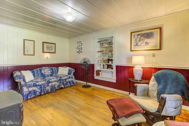 living room with wood finished floors, wooden walls, a wainscoted wall, built in shelves, and wood ceiling