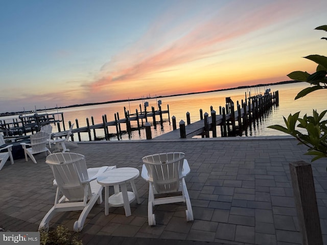 patio terrace at dusk featuring a water view and a dock
