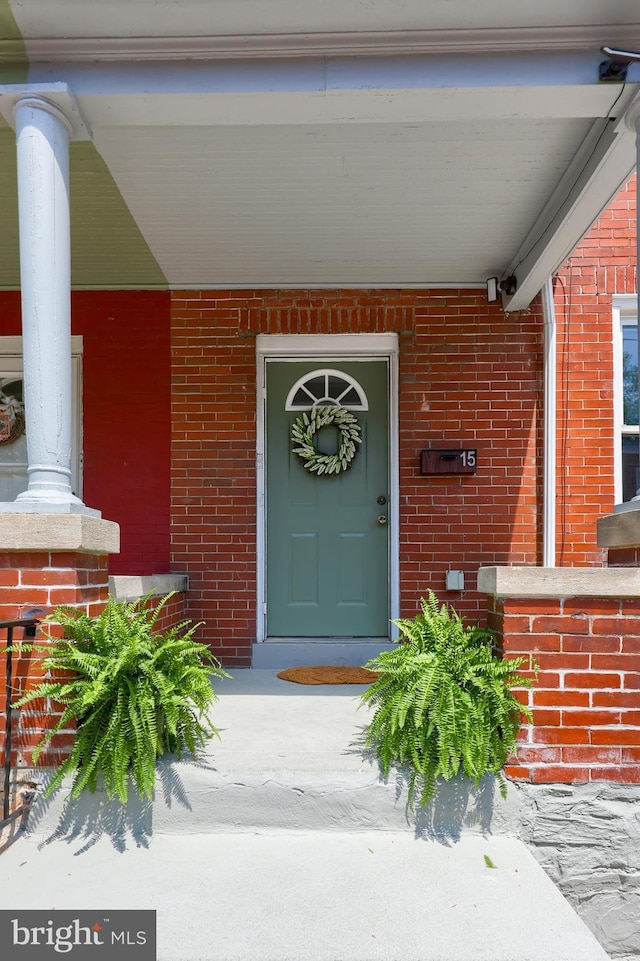 view of exterior entry featuring covered porch and brick siding