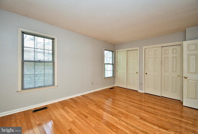 unfurnished bedroom with light wood-type flooring, multiple closets, baseboards, and multiple windows