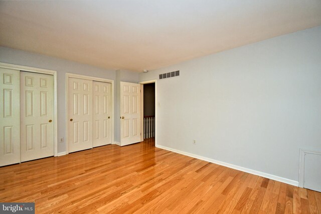 unfurnished bedroom with visible vents, light wood-style flooring, multiple closets, and baseboards