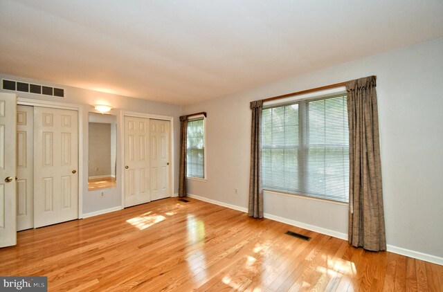unfurnished bedroom featuring two closets, baseboards, visible vents, and light wood-style floors