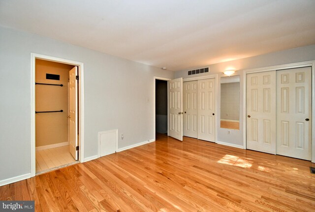 unfurnished bedroom featuring multiple closets, baseboards, light wood-type flooring, and visible vents