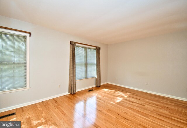 empty room with baseboards, visible vents, and light wood finished floors