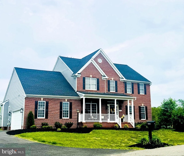 view of front of property with a front yard, brick siding, covered porch, and aphalt driveway