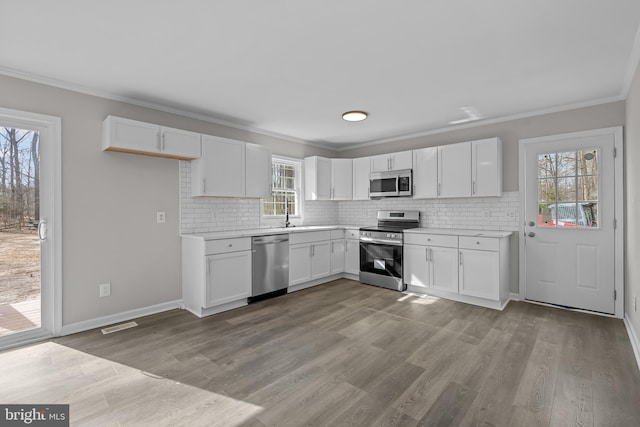 kitchen with appliances with stainless steel finishes, white cabinetry, and ornamental molding
