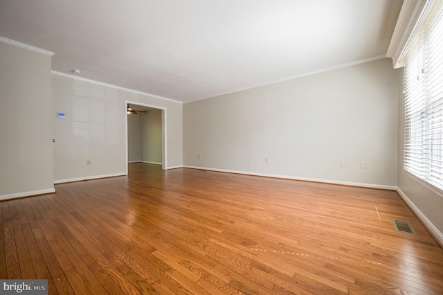 empty room with crown molding, ceiling fan, wood-type flooring, baseboards, and visible vents