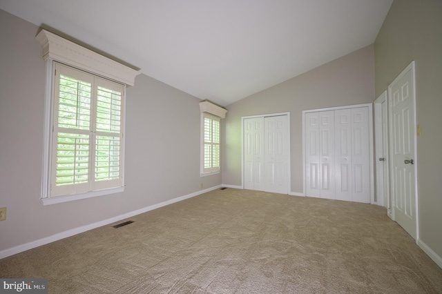 unfurnished bedroom featuring visible vents, lofted ceiling, two closets, and multiple windows