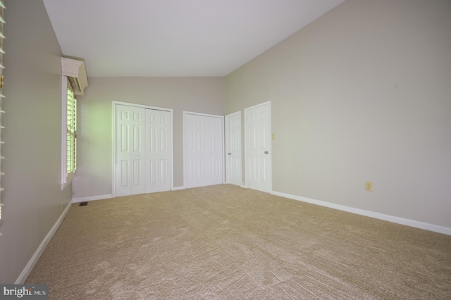 unfurnished bedroom featuring baseboards, multiple closets, light carpet, and high vaulted ceiling