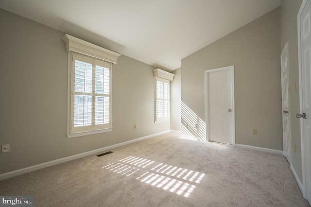 carpeted spare room featuring visible vents, baseboards, and vaulted ceiling