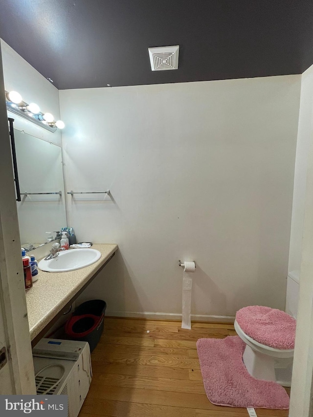 half bath with toilet, wood finished floors, vanity, and baseboards