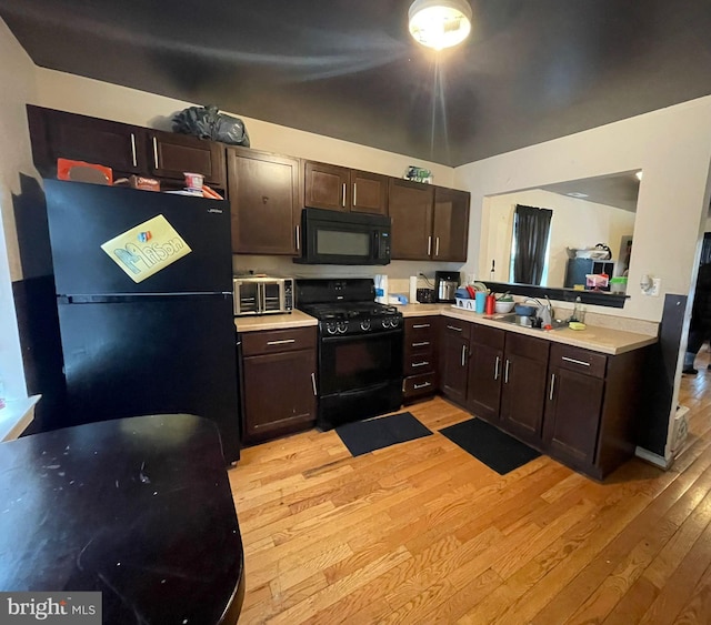 kitchen with a sink, light wood-style floors, black appliances, dark brown cabinetry, and light countertops