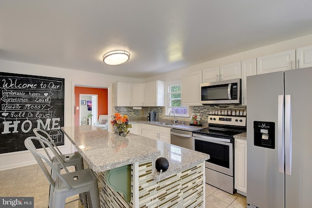 kitchen with white cabinets, a sink, appliances with stainless steel finishes, light tile patterned flooring, and backsplash