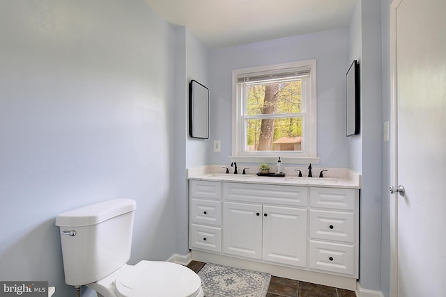 bathroom with baseboards, toilet, double vanity, and a sink